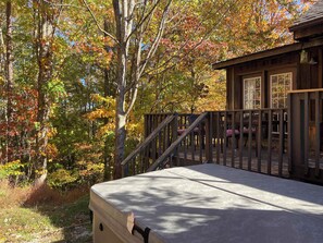 A wooden deck with a concrete floor, surrounded by trees with autumn foliage. - Pine Cove - Hot Tub - Pet Friendly - Large Yard (Campton)