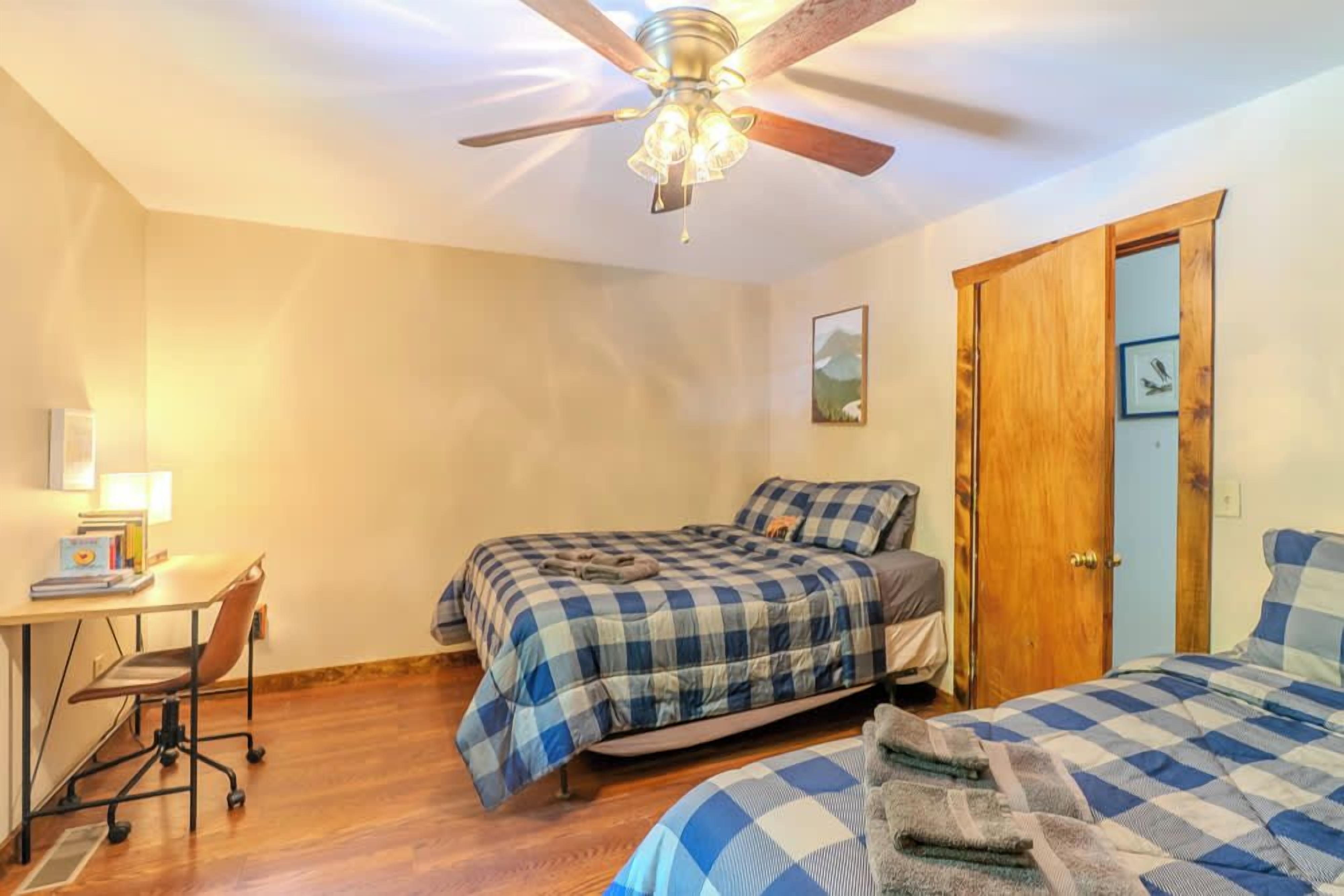 A bedroom with two beds, a desk, a chair, and a ceiling fan.