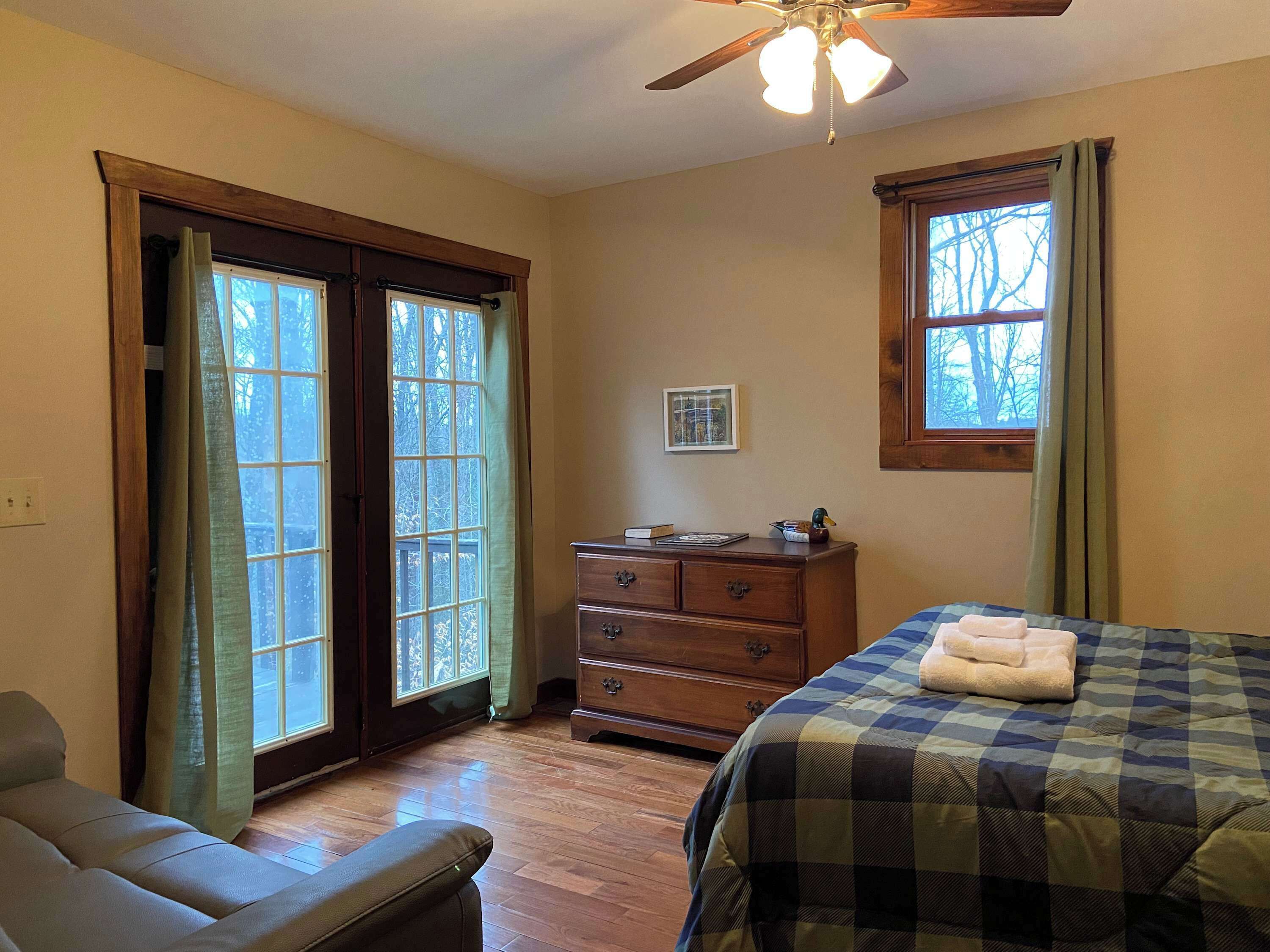 A bedroom with a bed, a dresser, a ceiling fan, and a window with curtains.