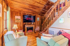 A cozy living room with a fireplace, a television, and a staircase. - Pine Cove - Hot Tub - Pet Friendly - Large Yard (Campton)