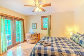 Une chambre à coucher avec un lit, une commode, un ventilateur de plafond et une fenêtre avec des rideaux.