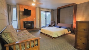 Un dormitorio con cama, sofá, chimenea, televisión y vistas al exterior.