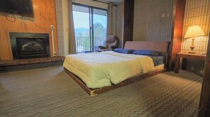 Un dormitorio con una cama grande, chimenea, una silla y vistas al exterior.