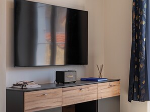 A modern room with a flat-screen TV mounted on the wall, a small black speaker, and a wooden cabinet with drawers. - Cosy 2-Br Apartment - Cannes City Centre (Cannes)