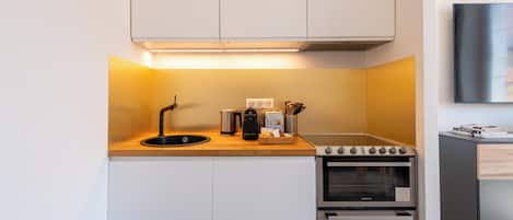 Una kitchenette compacta con horno integrado, un lavamanos y una cafetera.