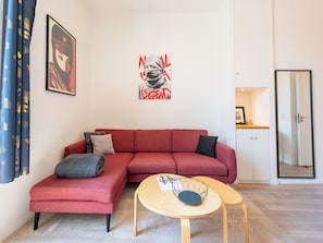 A modern living room with a red sectional sofa, a small round table, and a wall-mounted artwork. - Cosy 2-Br Apartment - Cannes City Centre (Cannes)