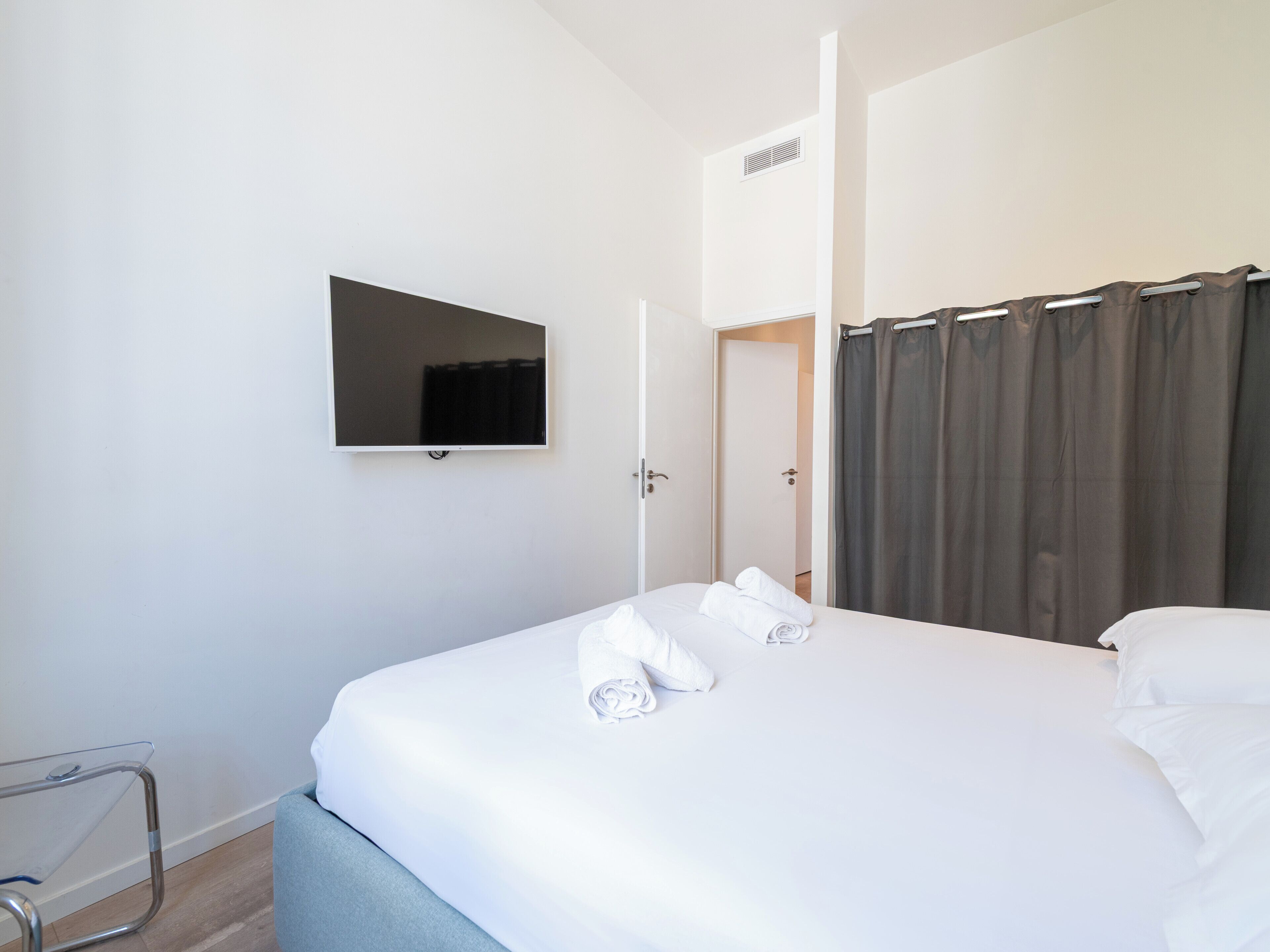 Quarto de hotel com cama, televisão de tela plana na parede e porta que dá para outro quarto.
