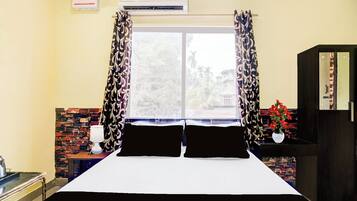 Habitación de hotel con cama, cortinas, ventana, pared de ladrillo, mesita de noche, lámpara y armario.