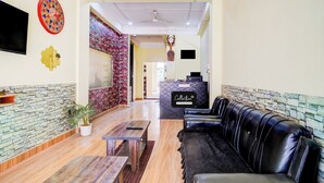 Un hall de hotel con mostrador de recepción, un sofá de cuero negro, un televisor montado en la pared y una pared decorativa con un reloj.