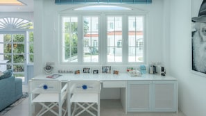 Ein helles Zimmer mit einem großen Fenster, einem weißen Schreibtisch, zwei weißen Stühlen und einer Heizung.