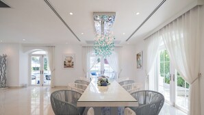 A spacious dining area with a long table, white chairs, and a decorative chandelier. - Villa Carpe Diem by Elite Havens (Natai)