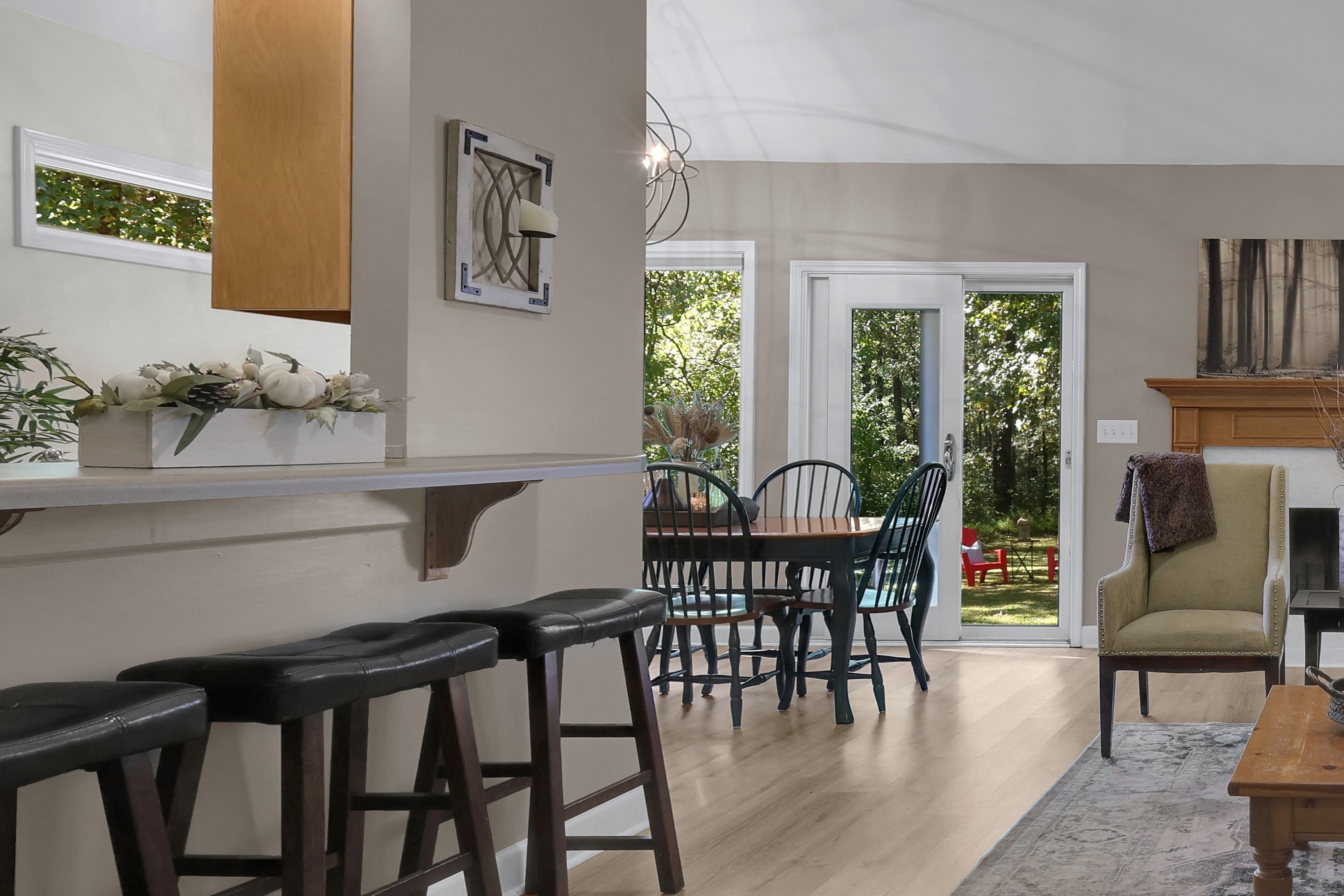 A dining area with a wooden table and chairs, a bar with stools, and a view of the outdoors through a glass door.