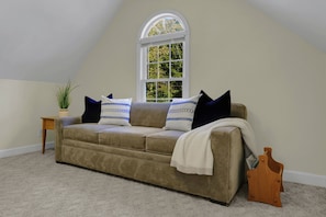 A room with a brown sofa, a small side table, a potted plant, and a window with a view of greenery. - Comfy wooded country house close from Nashville. (Nashville)