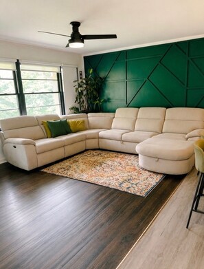 A modern living room with a sectional sofa, a patterned rug, and a green accent wall. - Emerald Retreat - Modern 3 Bedroom Near Atlanta (Austell)