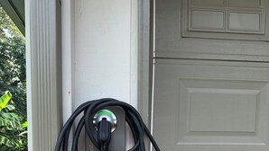 A power outlet with a charging cable plugged in, attached to a white wall. - Emerald Retreat - Modern 3 Bedroom Near Atlanta (Austell)