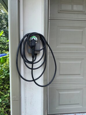 A power outlet with a charging cable plugged in, attached to a white wall. - Emerald Retreat - Modern 3 Bedroom Near Atlanta (Austell)