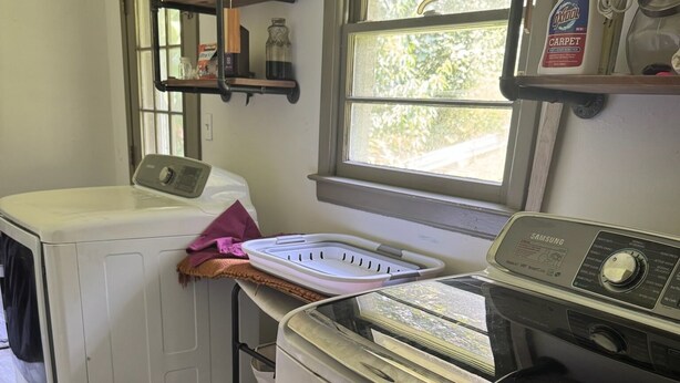 A laundry room with a front-loading washer and dryer, a drying rack, and a window with a view of greenery outside. - Emerald Retreat - Modern 3 Bedroom Near Atlanta (Austell)