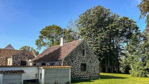 Um edifício de pedra com telhado de telhas, cercado por grama e árvores.