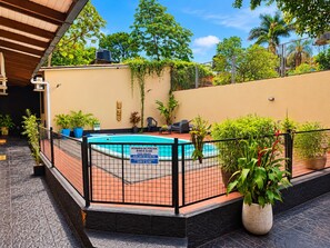 A swimming pool area with a fence, potted plants, and a sign indicating pool hours.