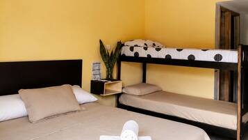 Habitación con dos camas, una con una colcha de lunares y la otra de color liso. Hay una planta pequeña en una mesita de noche y una toalla enrollada sobre la cama.