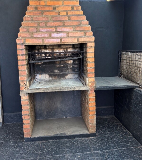 A brick-built outdoor oven with a metal shelf, set against a dark wall and tiled floor.