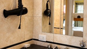 Un baño con espejo, lavamanos, secador de pelo y toallero.