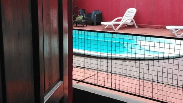 Un área de piscina con suelo de baldosas, dos sillas reclinables blancas y una pared roja.