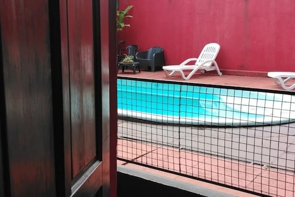 A pool area with a tiled floor, two white lounge chairs, and a red wall.