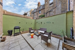 Eine Terrasse mit Gartenmöbeln, einem Grill und einer grünen Wand mit dem Schriftzug 'CHILL'.