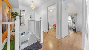 En modern inredning med en trappa, trägolv och utsikt över ett sovrum med ett rött sängöverkast.