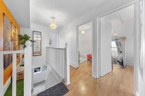 Ein modernes Interieur mit Treppe, Holzboden und Blick in ein Schlafzimmer mit rotem Überwurf.
