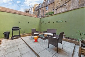 Un espace patio aménagé avec du mobilier d’extérieur, une poubelle et un panneau indiquant « HEURE HEUREUSE ».