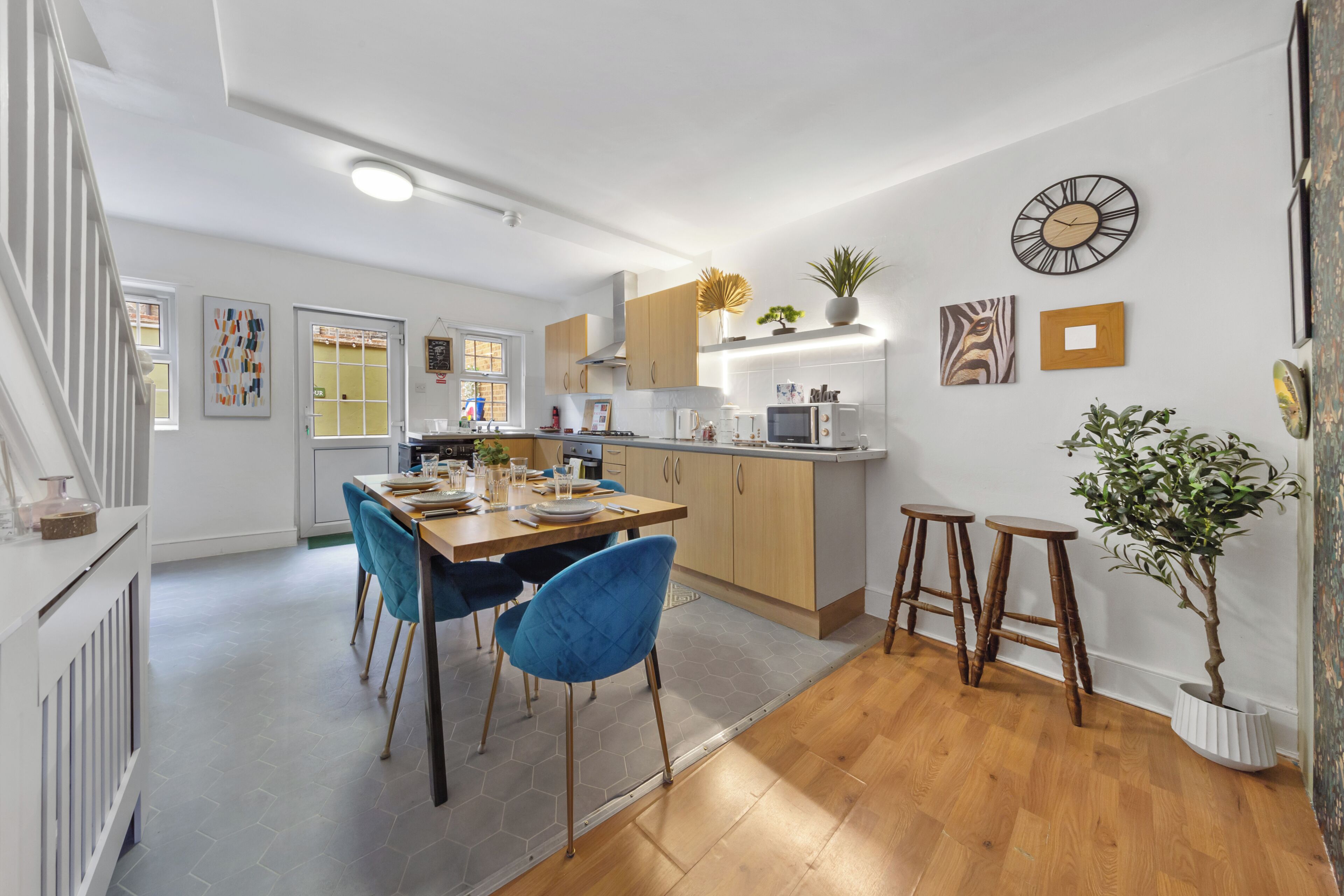 A modern kitchen with a dining area, wooden flooring, and a staircase leading to another level.