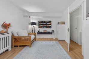 Ein modernes Wohnzimmer mit einem Holzsofa, einer weißen Kommode, einem Wand-Fernseher und einem kleinen Tisch mit Dekoration.
