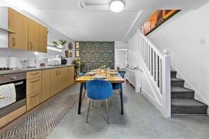 Eine moderne Küche mit Holzschränken, ein Essbereich mit blauen Stühlen und eine Treppe.