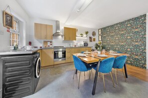 A modern kitchen with a dining area, featuring a stainless steel range hood, wooden cabinets, and a patterned wallpaper. - STUNNING Home in the Heart of Whitechapel - Minutes from Central London (London)