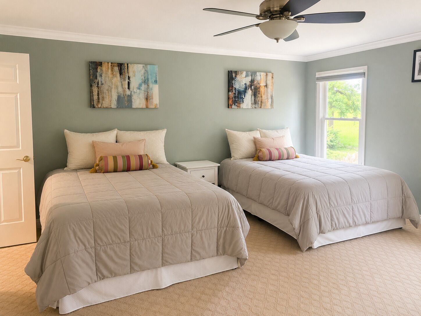 Une chambre avec deux lits, un ventilateur de plafond et des œuvres d’art accrochées aux murs.