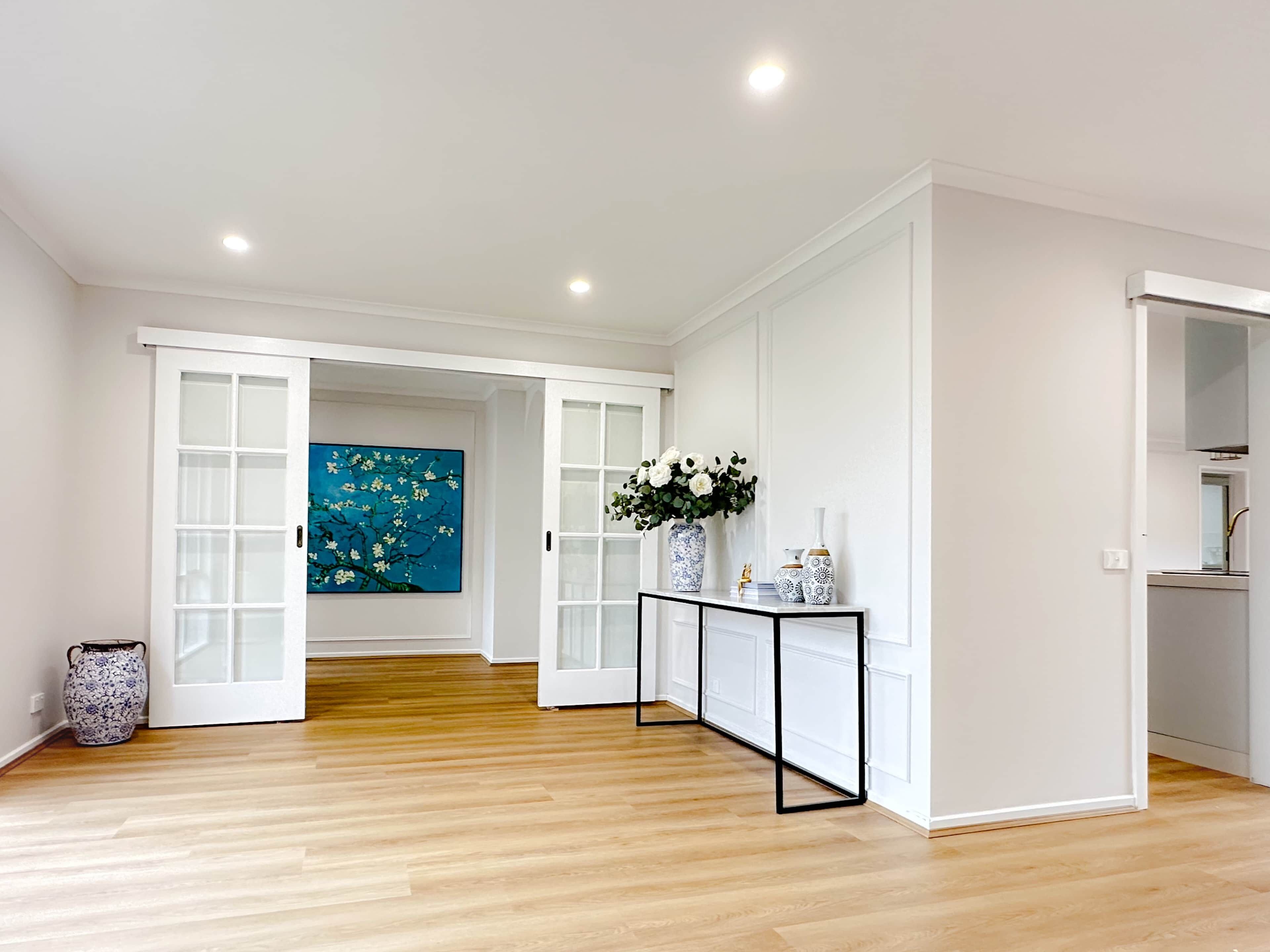 Een hal met houten vloer, witte muren en een console tafel met decoratieve objecten.