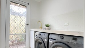 A laundry room with a front-loading washing machine and a sink. - Shine Adam Court - Prestige Retreat in Pakenham (Pakenham)