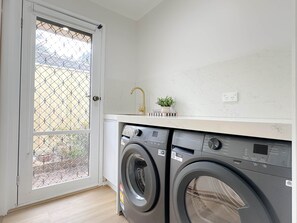A laundry room with a front-loading washing machine and a sink. - Shine Adam Court - Prestige Retreat in Pakenham (Pakenham)