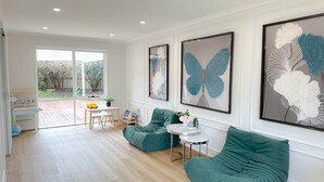A spacious living area with a green sofa, a small round table, and a dining table with chairs. There are large framed butterfly artworks on the wall. - Shine Adam Court - Prestige Retreat in Pakenham (Pakenham)