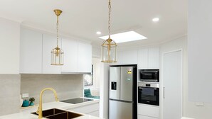 A modern kitchen with white cabinetry, a stainless steel refrigerator, a built-in oven, and a sink with a gold faucet. - Shine Adam Court - Prestige Retreat in Pakenham (Pakenham)