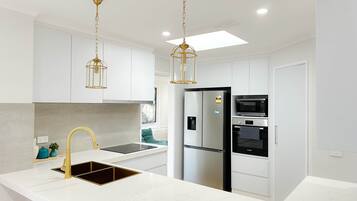 A modern kitchen with white cabinetry, a stainless steel refrigerator, a built-in oven, and a sink with a gold faucet.