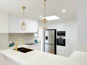A modern kitchen with white cabinetry, a stainless steel refrigerator, a built-in oven, and a sink with a gold faucet. - Shine Adam Court - Prestige Retreat in Pakenham (Pakenham)
