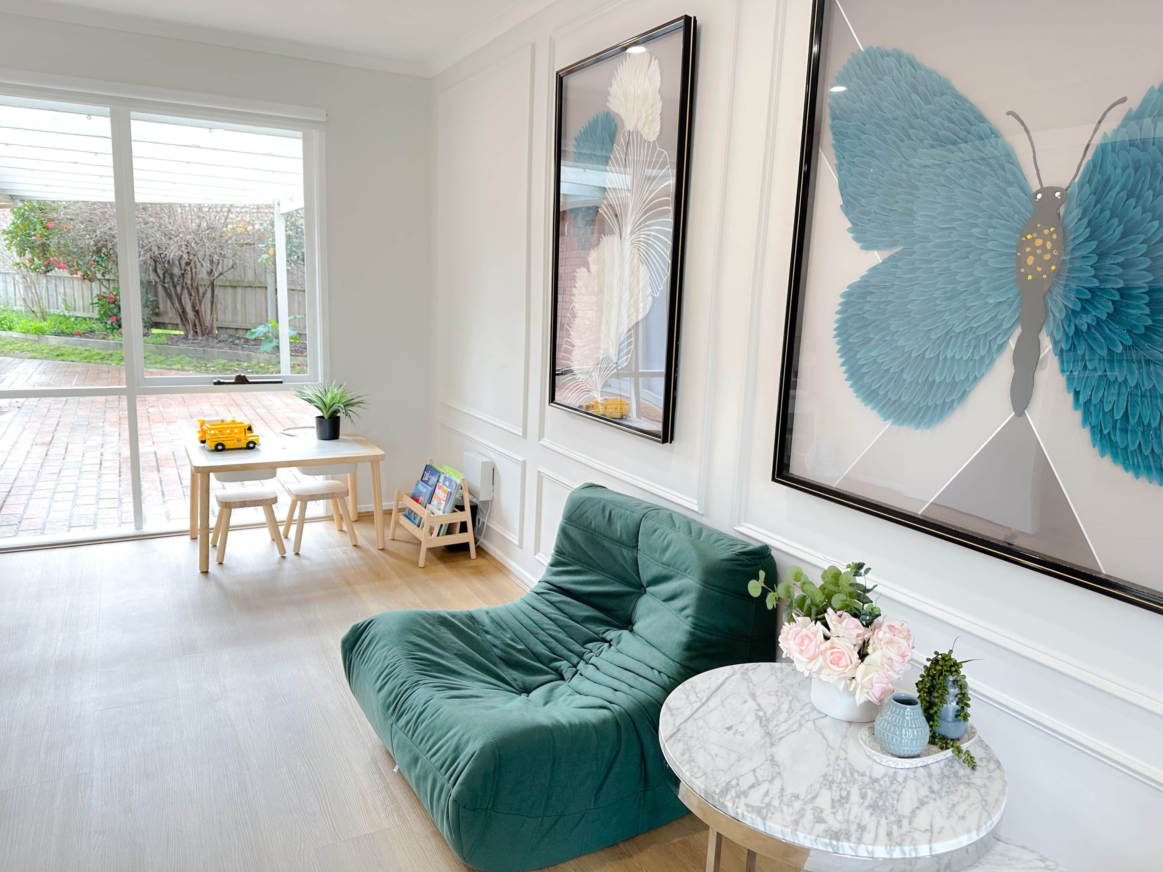 Um quarto com um sofá verde, uma mesa redonda pequena com flores e uma janela com vista para um jardim.