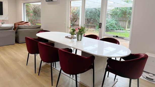A modern kitchen with a white marble countertop, red chairs, and a view of the backyard through large windows. - Shine Adam Court - Prestige Retreat in Pakenham (Pakenham)