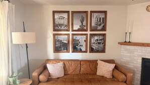 Una sala de estar con un sofá de cuero marrón, una mesa de centro y una chimenea. Seis fotografías blanco y negro enmarcadas adornan la pared.
