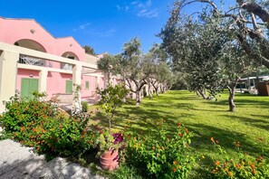 Um edifício rosa com varanda, cercado por um jardim bem cuidado com diversas plantas e flores.