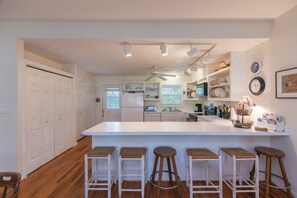 A kitchen with a central island, bar stools, white cabinetry, and a dining area. - Makin Time | Secluded Coastal Retreat | Easy Walk to Beach | Sleeps 8 | Dogs Welcome (Edisto Beach)