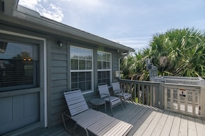 A covered outdoor area with a wooden deck, two lounge chairs, and a small table. - Makin Time | Secluded Coastal Retreat | Easy Walk to Beach | Sleeps 8 | Dogs Welcome (Edisto Beach)